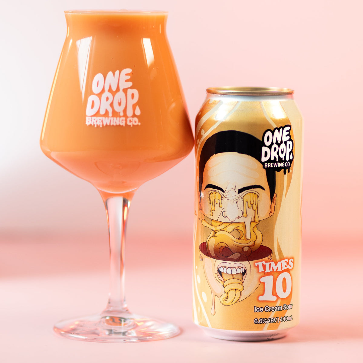 An orange ice cream sour glass and beside their can from One Drop Brewing Co., shown on a soft pink studio background.