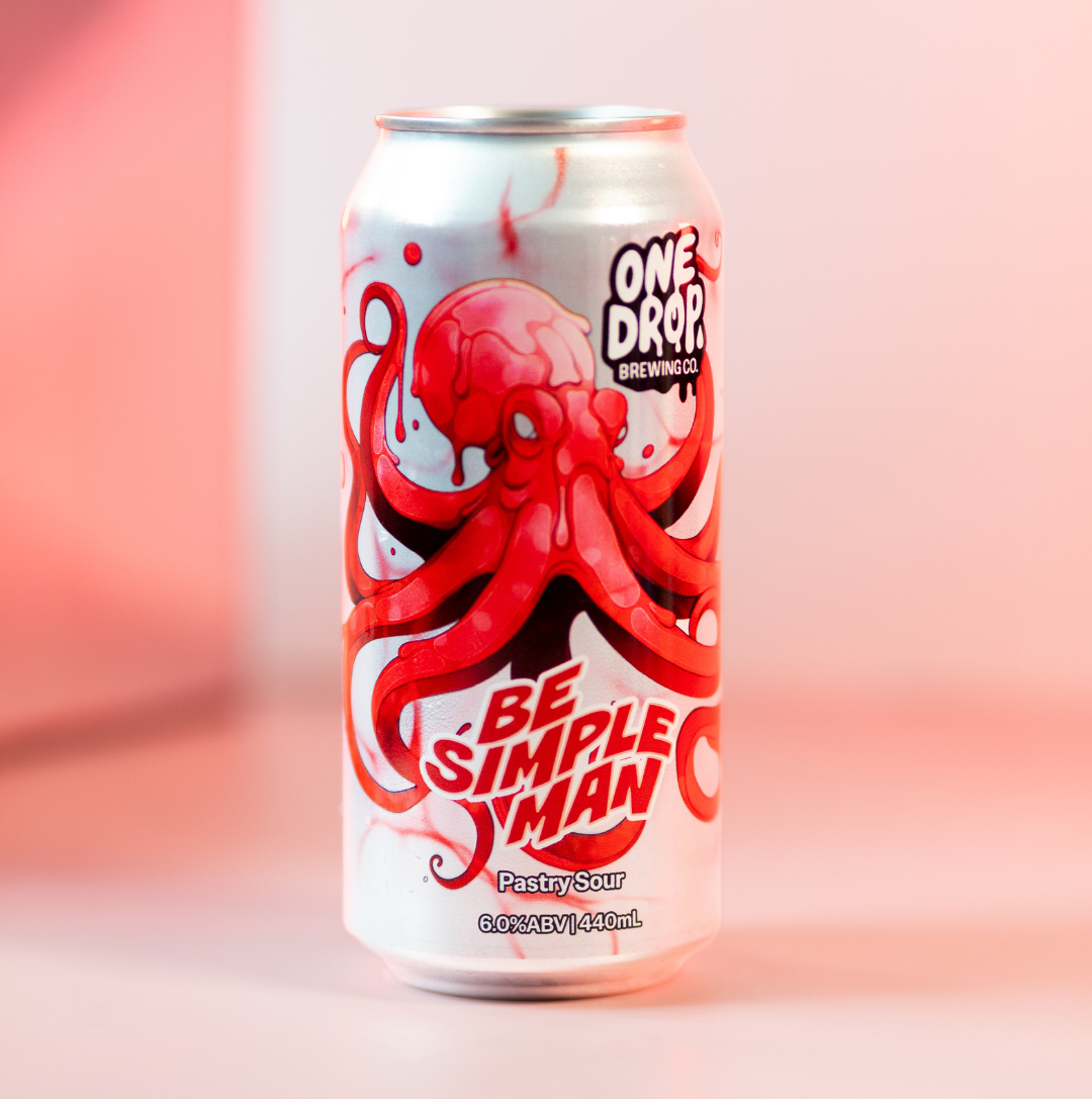 A single aluminum beverage can standing upright on a soft pink studio surface. The can is white with a large red octopus illustration and bold red text reading 'BE SIMPLE MAN,' plus 'ONE DROP BREWING CO' near the top.
