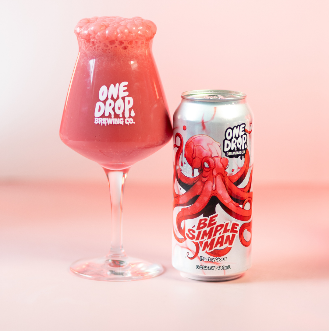 A pink beverage in a stemmed glass and a matching pink can from One Drop Brewing Co. The can features a red octopus illustration and the text 'BE SIMPLE MAN'.