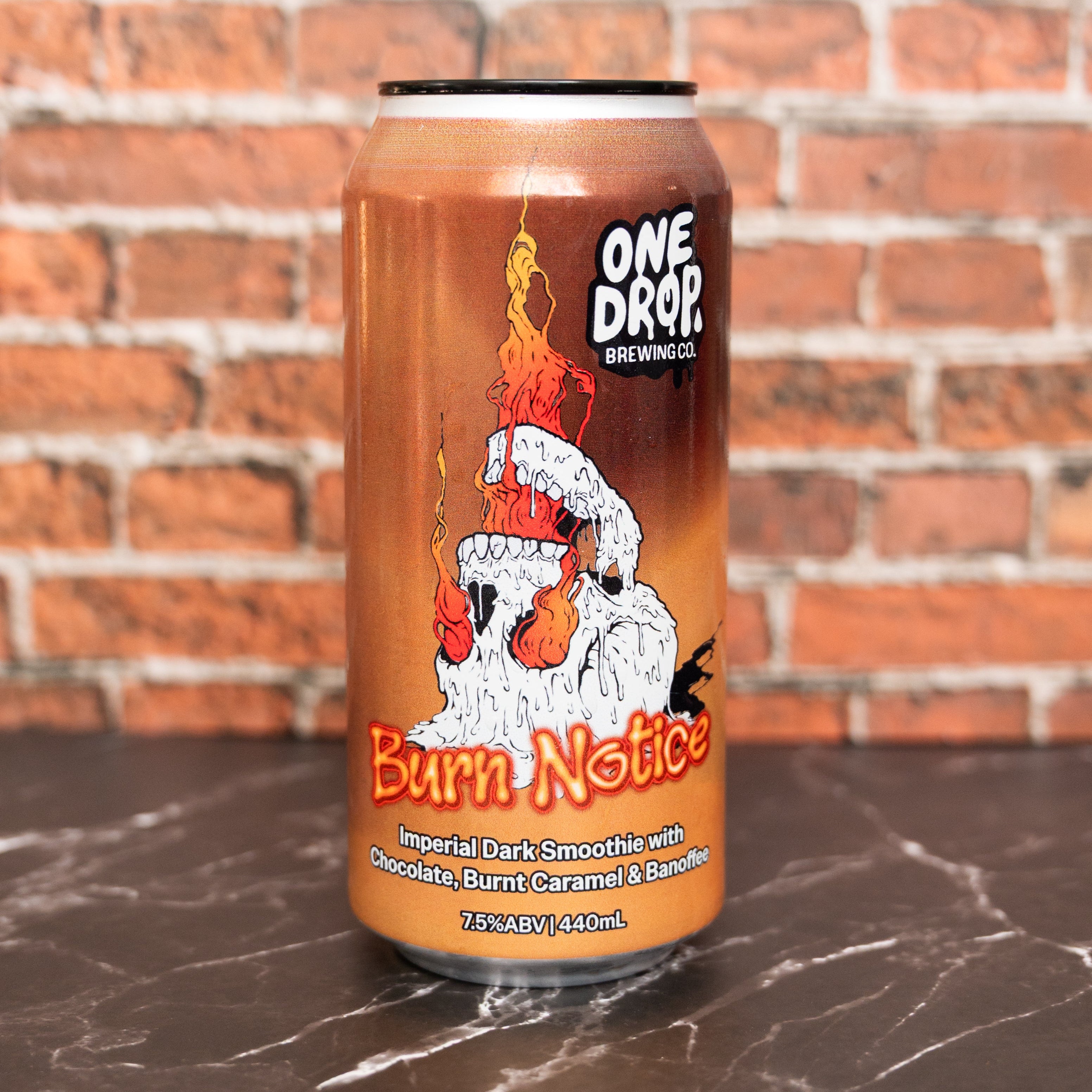 A 33cl aluminum can of One Drop Brewing's 'Burn Notice' Imperial Dark Smoothie, featuring a fiery orange and brown label with a white skull graphic, set on a dark marble surface against a red brick wall background.