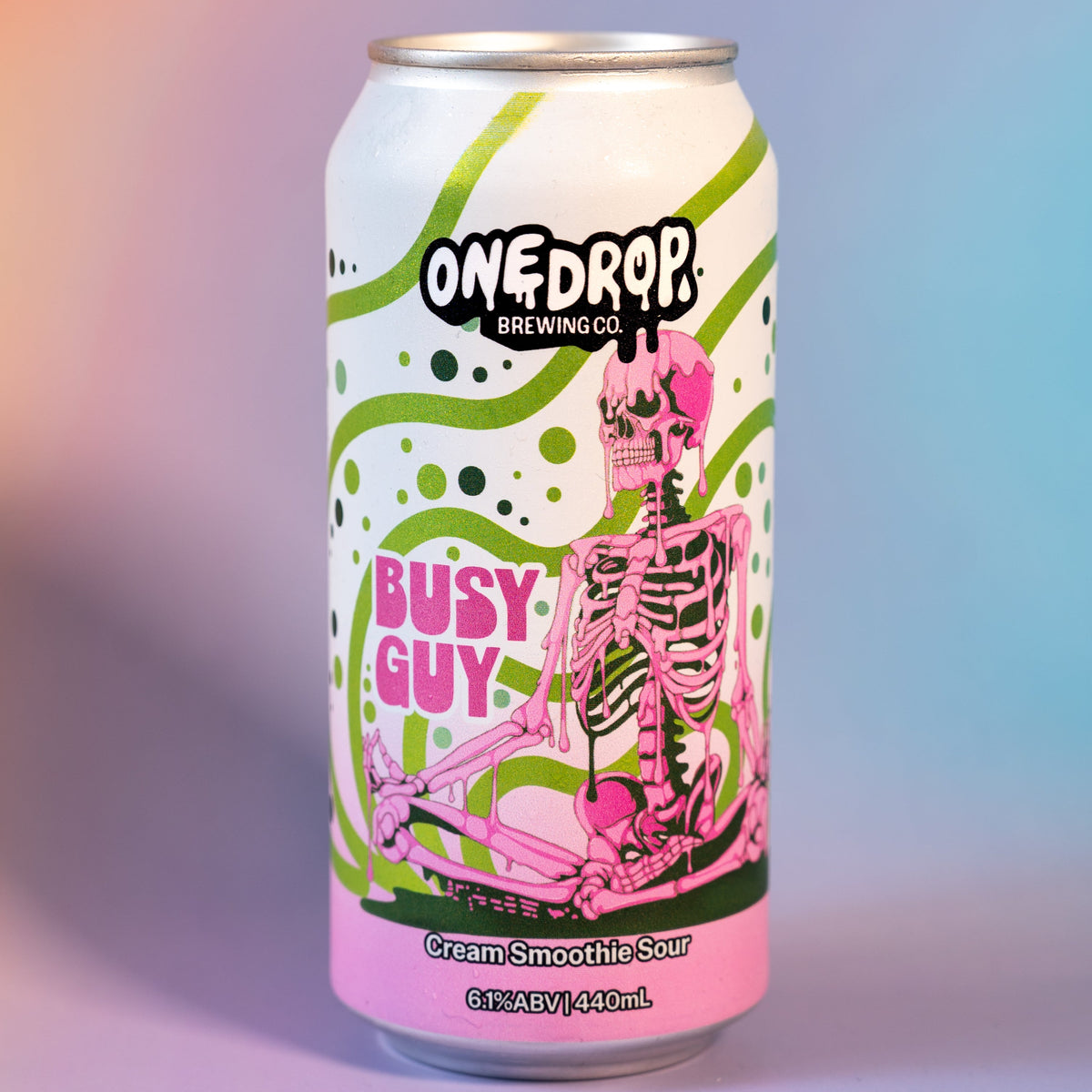 A 16 oz aluminum can of OneDrop Brewing's 'Busy Guy' sour draft beer, featuring a white label with a pink skeleton and green splatter details, set against a soft pink and blue gradient background.