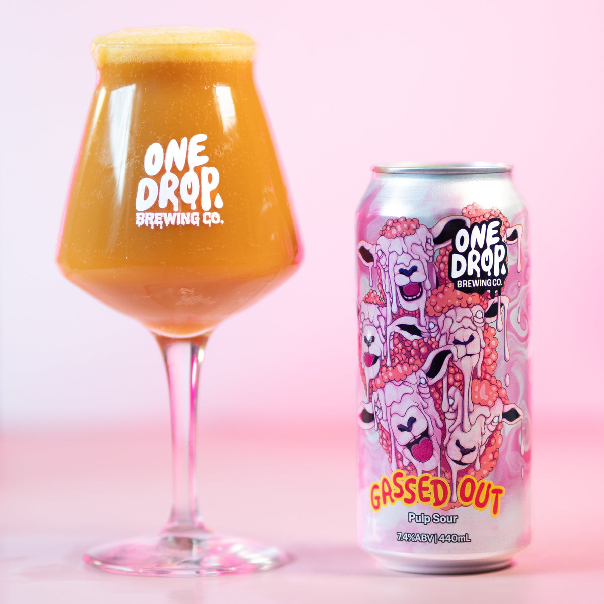 A glass of frothy orange beverage and a matching One Drop Brewery Co. can labeled 'Gassed Out' on a pink studio background.