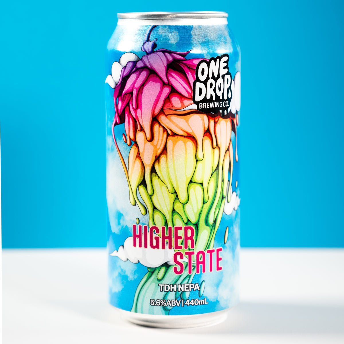 A 440mL aluminum can of One Drop Brewing's Higher State TDH NEPA beer, featuring a vibrant, colorful graphic of a flower on a blue sky background, set against a bright blue and white studio backdrop.