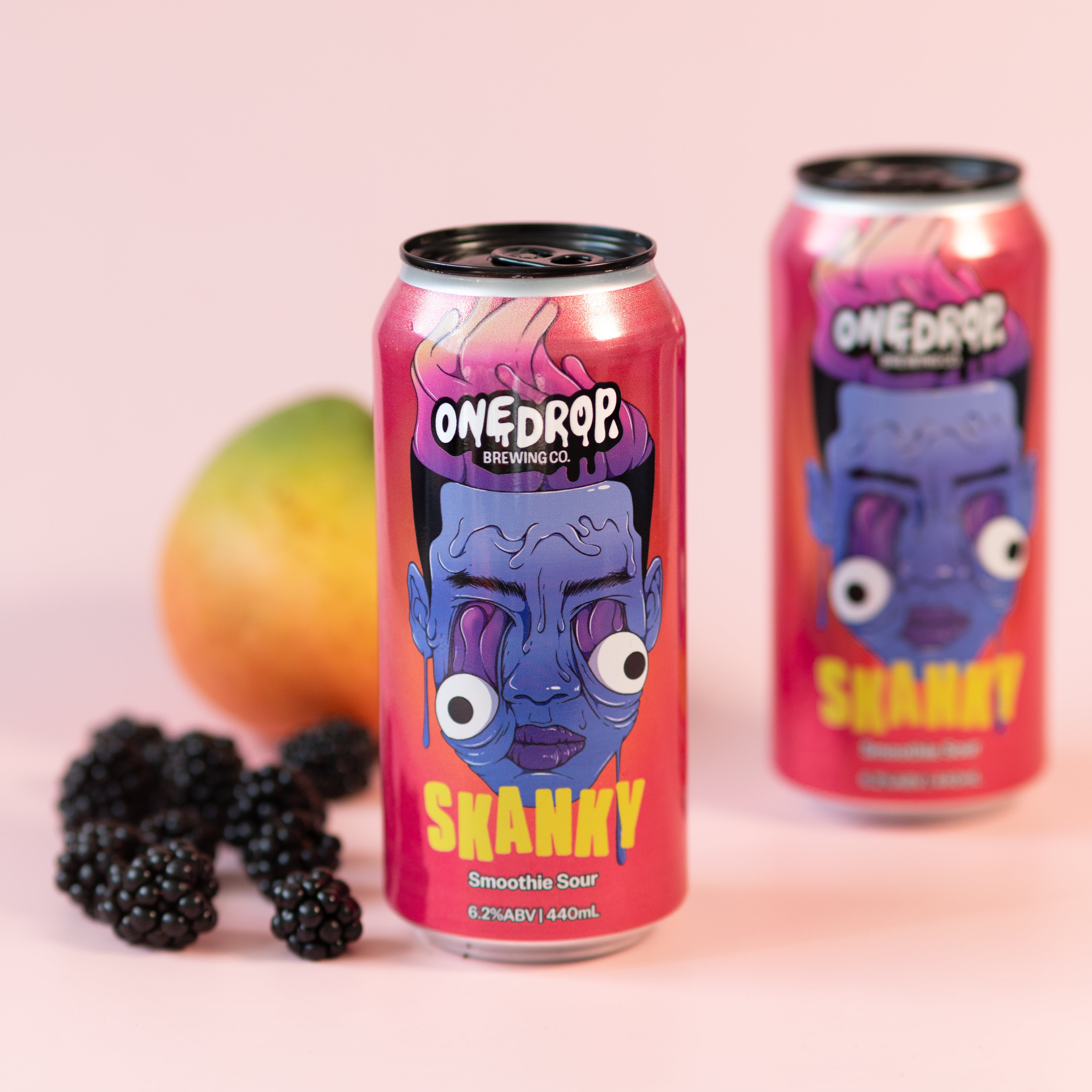 Two OneDrop Energy drinks, Shandy, in pink and purple cans, styled on a light pink background with a mango and blackberries.