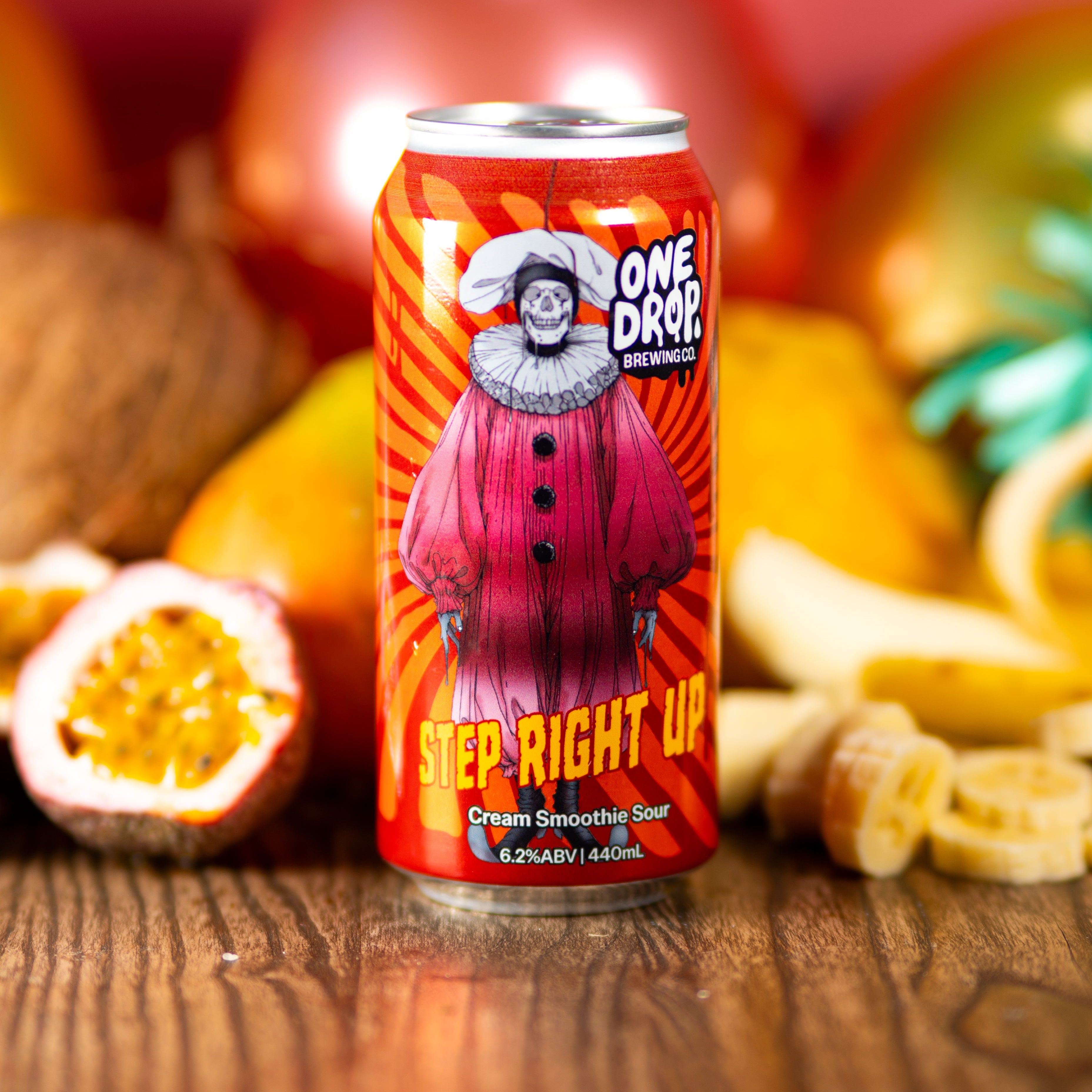 A can of One Drop Brewing 'Step Right Up' cream smoky sour beer stands on a wooden surface surrounded by fruit slices, a halved passion fruit, and decorative ornaments against a warm red background.