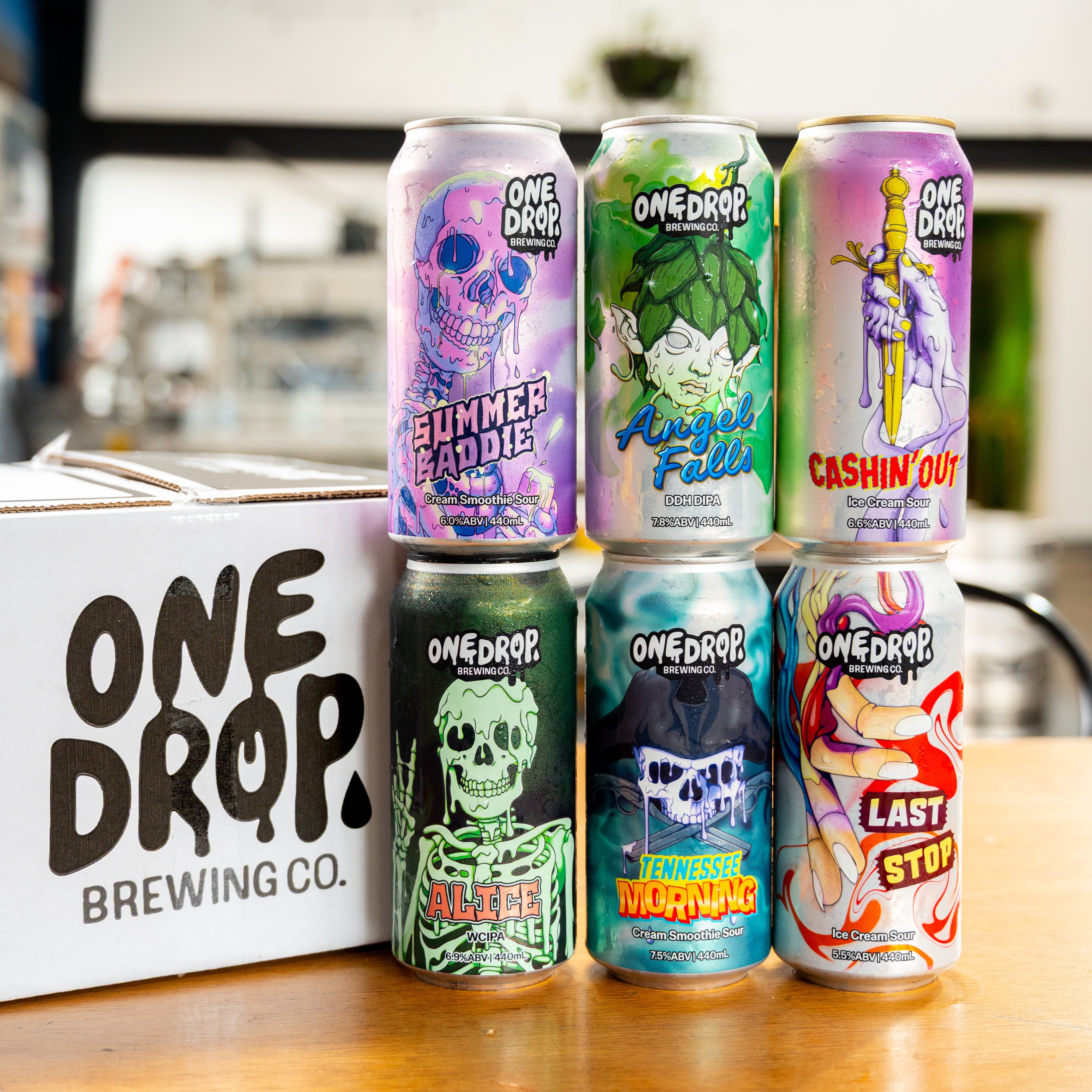 Collection of colorful beer cans from One Drop Brewing Co. on a wooden table.
