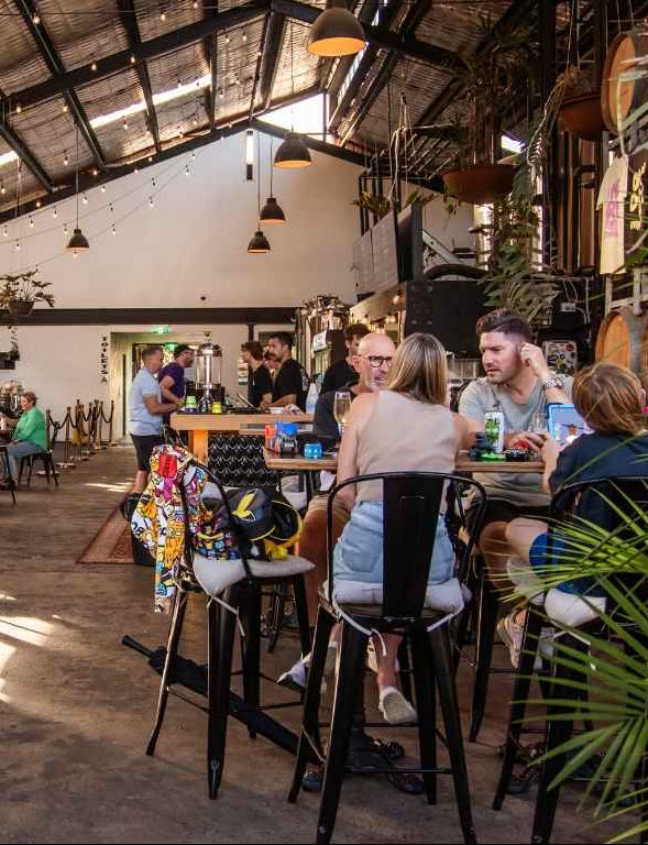 People sitting at tables in a ONE DROP setting with plants and hanging lights.
