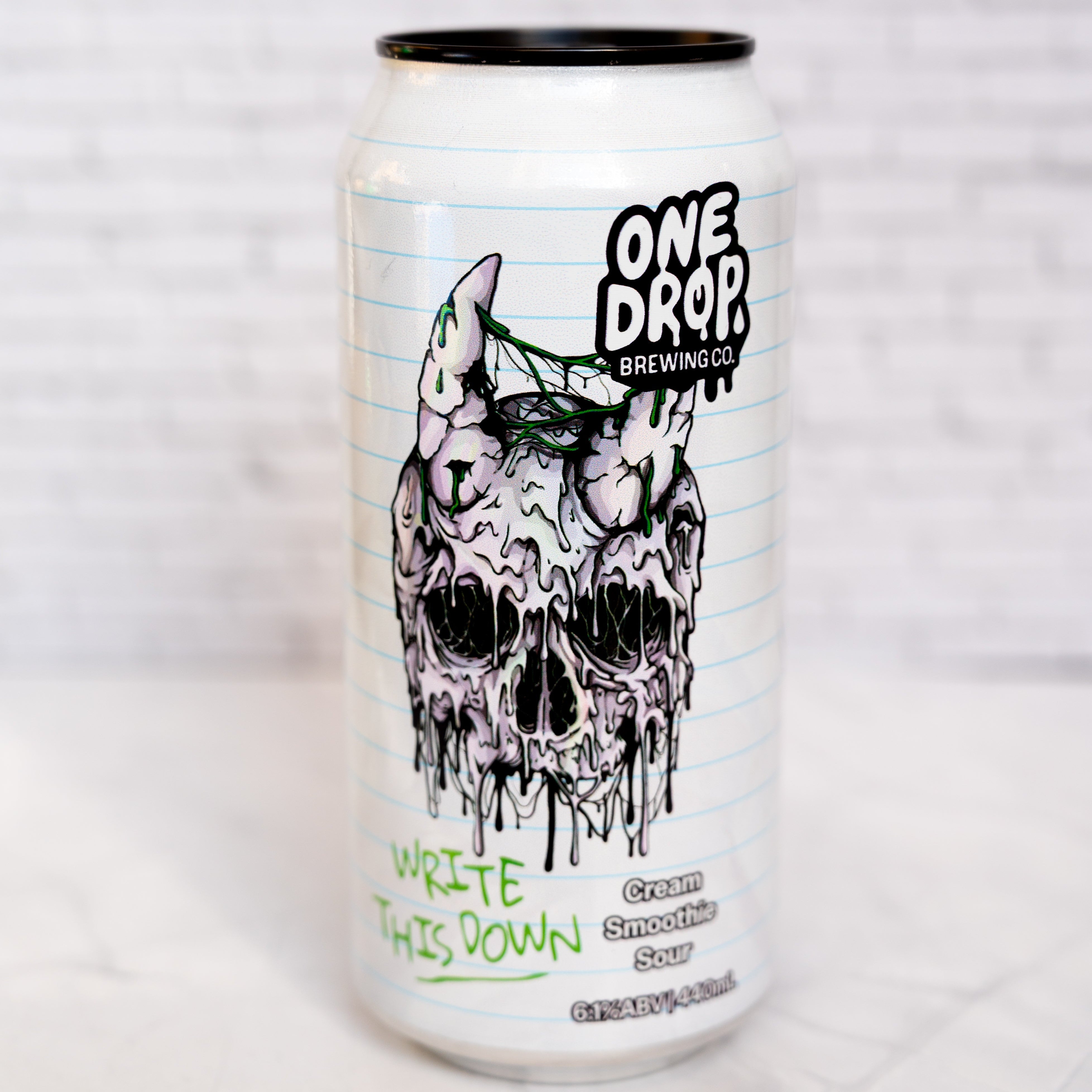 A 16 oz aluminum can of One Drop Brewing Co. Cream Smoothie Sour, featuring a white notebook-paper background with a black-and-white dripping skull illustration and green handwritten text, set against a white brick wall background.